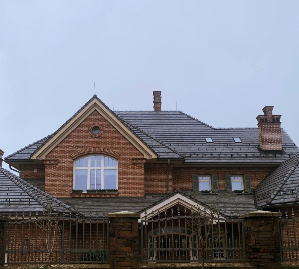 Elegant brick mansion with gabled roof and chimneys against a cloudy sky.